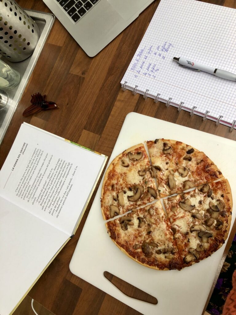 Een foto van de eettafel waar je pizza ziet en een leesboek in het Italiaans. Hier begon ons avontuur om de taal te leren.
